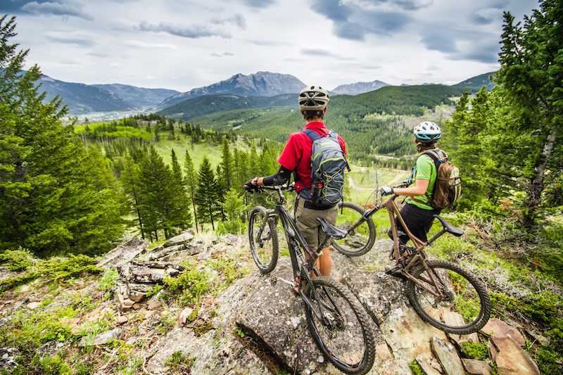 Two mountain bikers on a hilltop, looking out over a green mountain valley with blue sky overhead