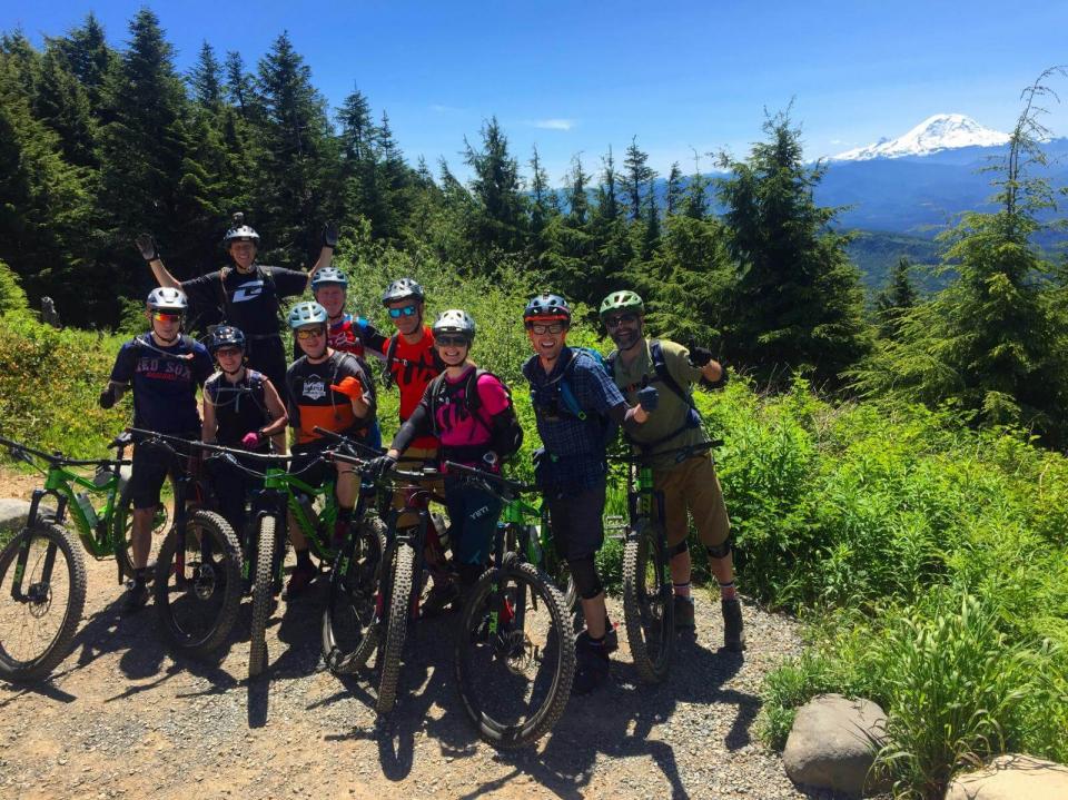 Group of mountain bikers in Seattle posing with their bikes on a grassy mountain field