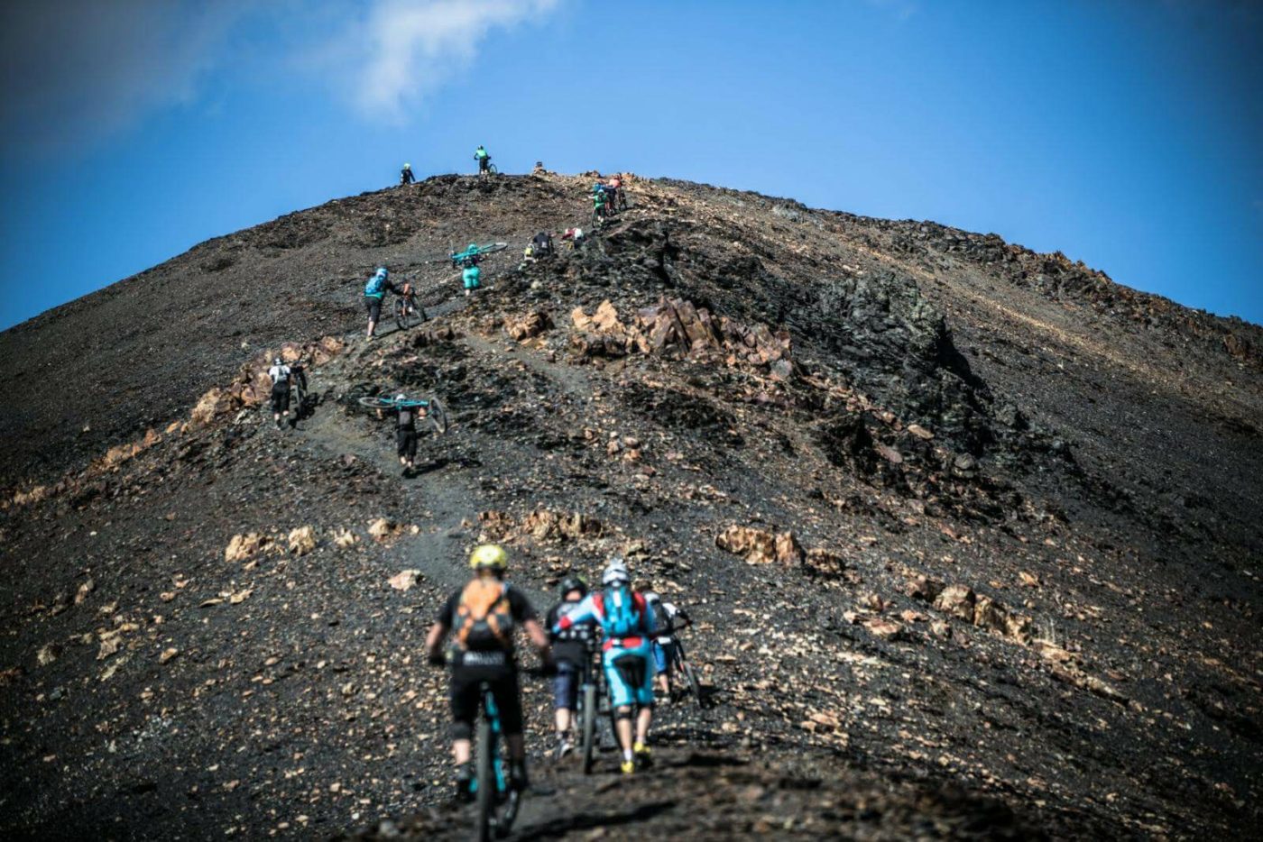 Several mountain bikers—some walking their bikes and some riding them—going up a steep dirt hill in the Pyrenees mountains in Spain.