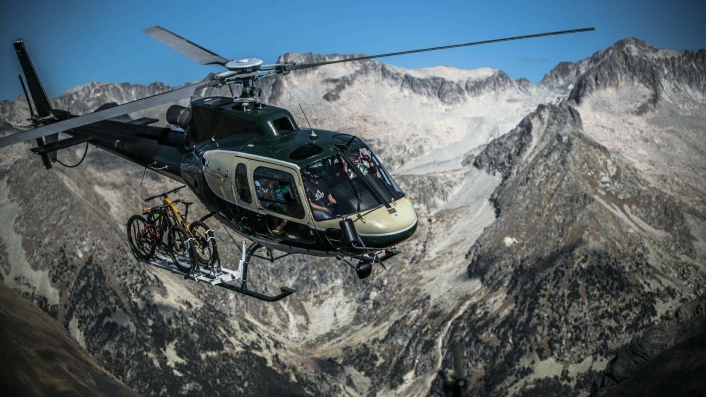 Helicopter carrying several mountain bikes flying over the mountains