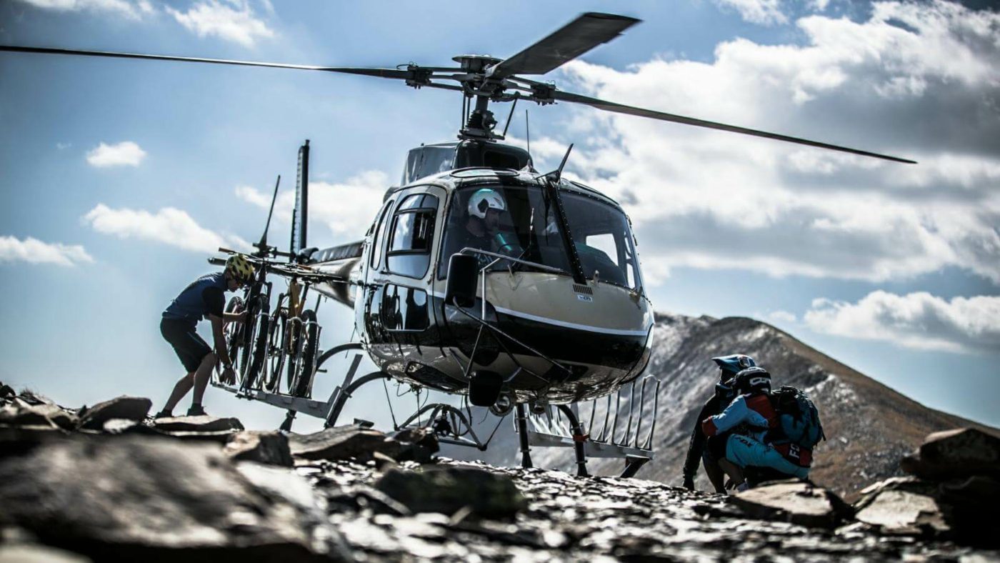 Helicopter that's landed on the mountain summit in the Pyrenees in Spain. Two people are pulling mountain bikes off the side bike racks.