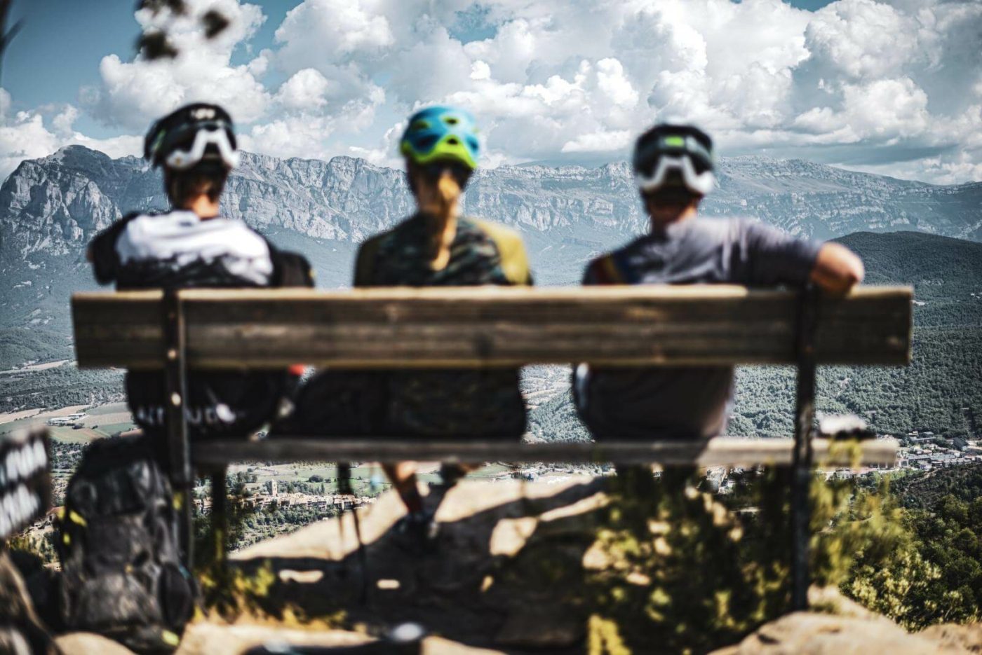 Three mountain bikers sitting on a bench as they look out over a valley in Spain.