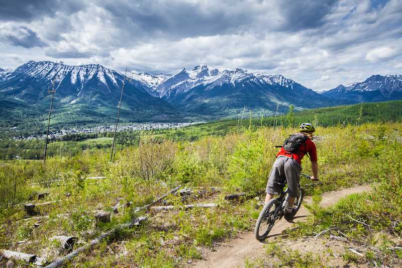 Mountain Biker riding across trail in wide, green field with mountain in the distance