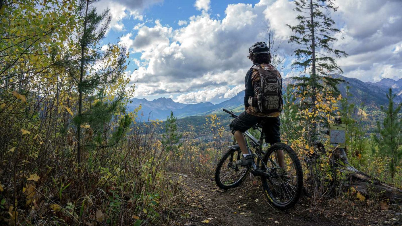 Person sitting still on their mountain bike at a mountain lookout with mountain valley in distance and blue sky overhead 