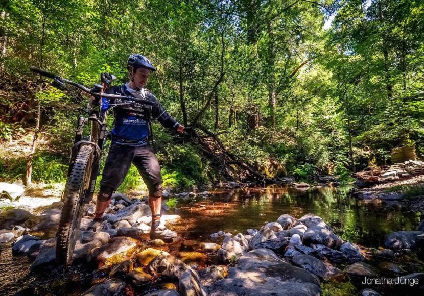 Mountain Biker walking bike across rocky part of shallow stream