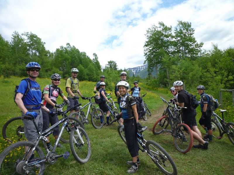 Several smiling mountain bikers standing next to their bikes in a grassy field.