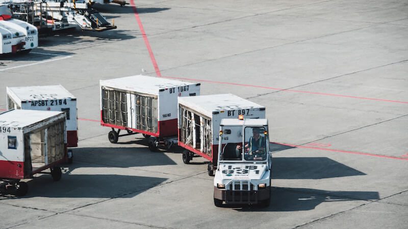 White airport luggage vehicle pulling two carts full of luggage on tarmac