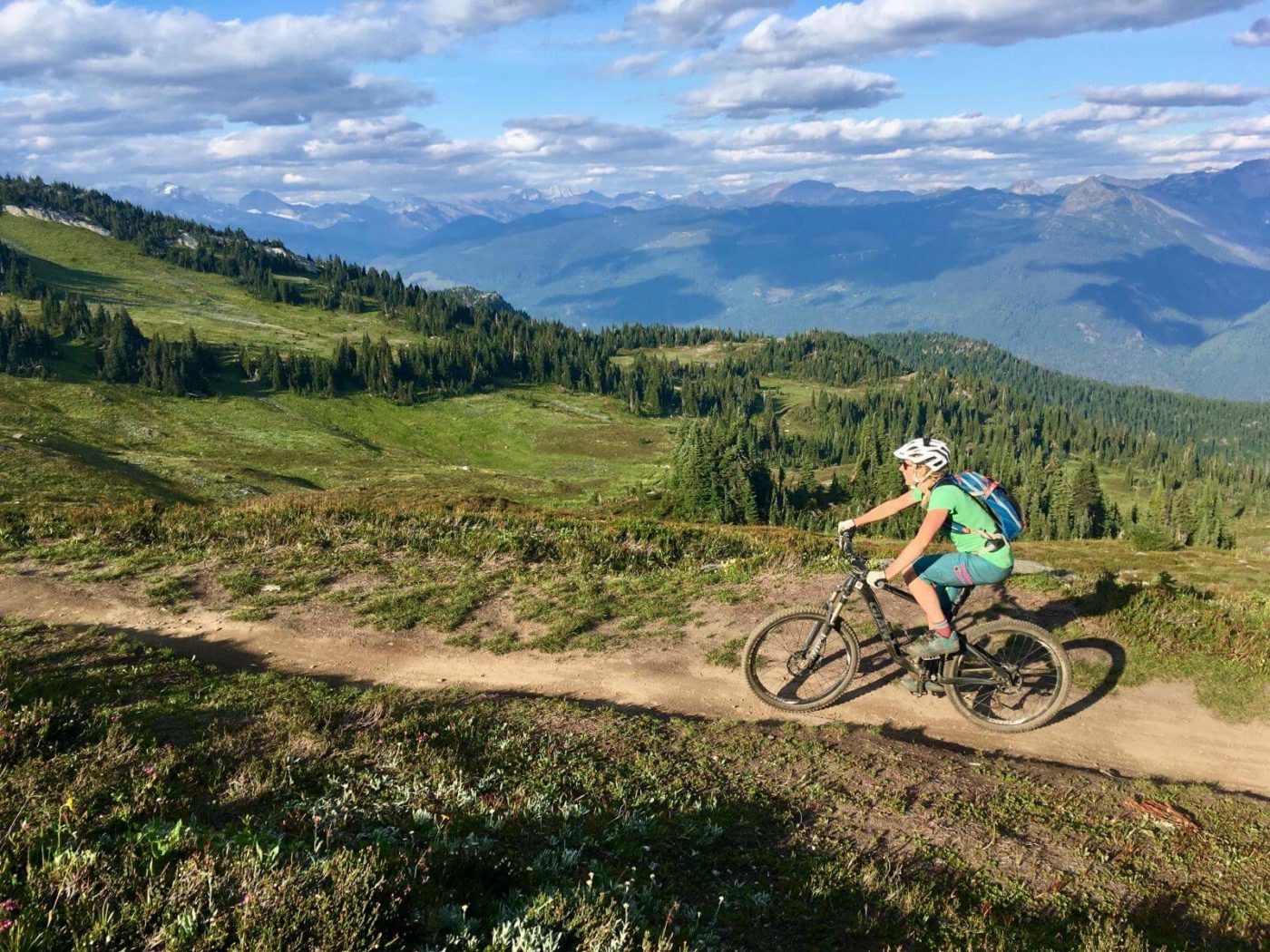 Woman on a mountain bike riding along a ridge trail overlooking mountains and green valley