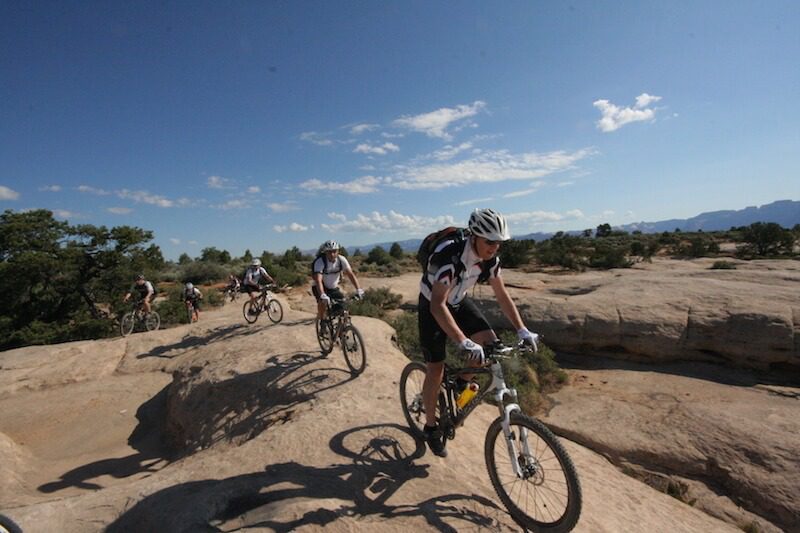 Mountain Bikers riding over red, rocky hills under a bright blue sky