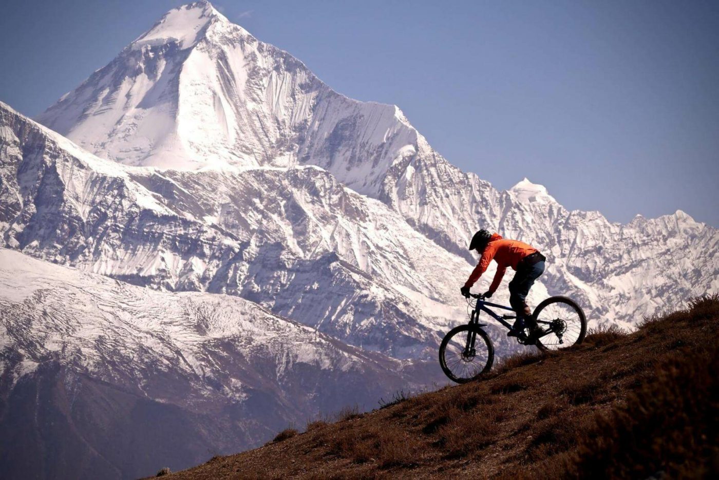 Mountain Biker going down a steep hill with snow-covered mountain in the background