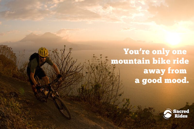 Man mountain biking along a ridge line at sunset near the ocean with the words, "You're only one mountain bike ride away from a good mood."