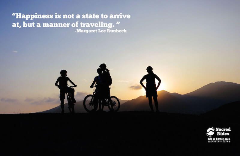 Silhouettes of three mountain bikers on a hilltop at sunset with the words, "Happiness is not a state to arrive at, but a manner of traveling. - Margaret Lee Runbeck