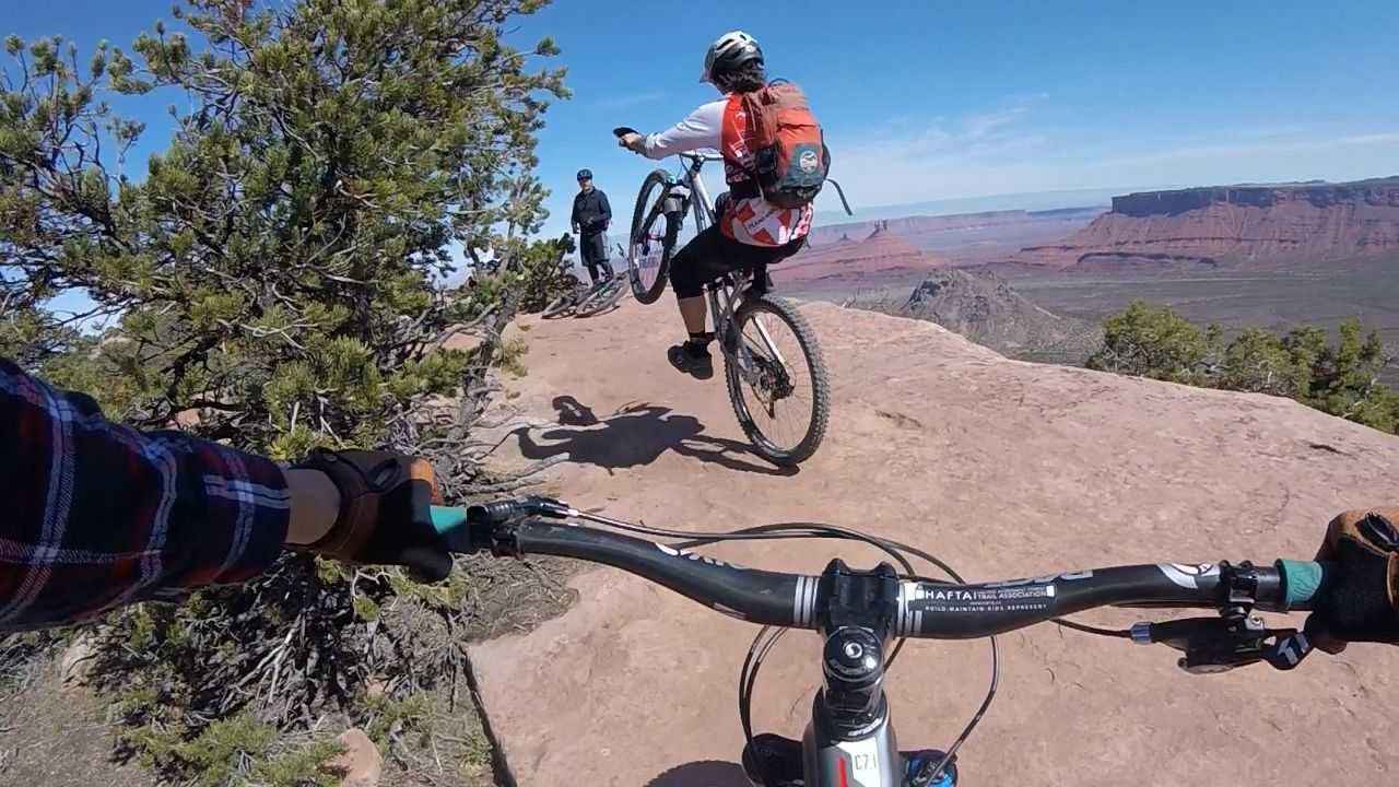 Looking over mountain bike handlebars at two other riders going over large, red rocks