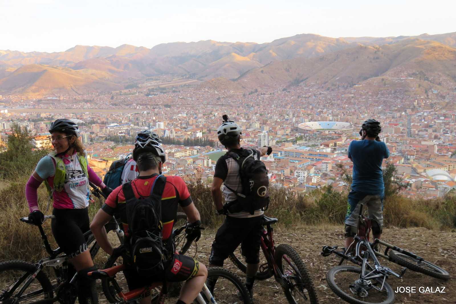 Five mountain bikers sitting on bikes high up on a hill, looking out over the red tile roofs in the valley below